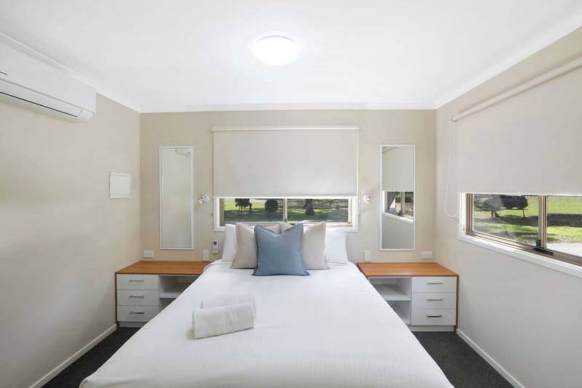 A bedroom with a large bed, a bedside table, a dresser, a window with a view of the outdoors, and a ceiling light.