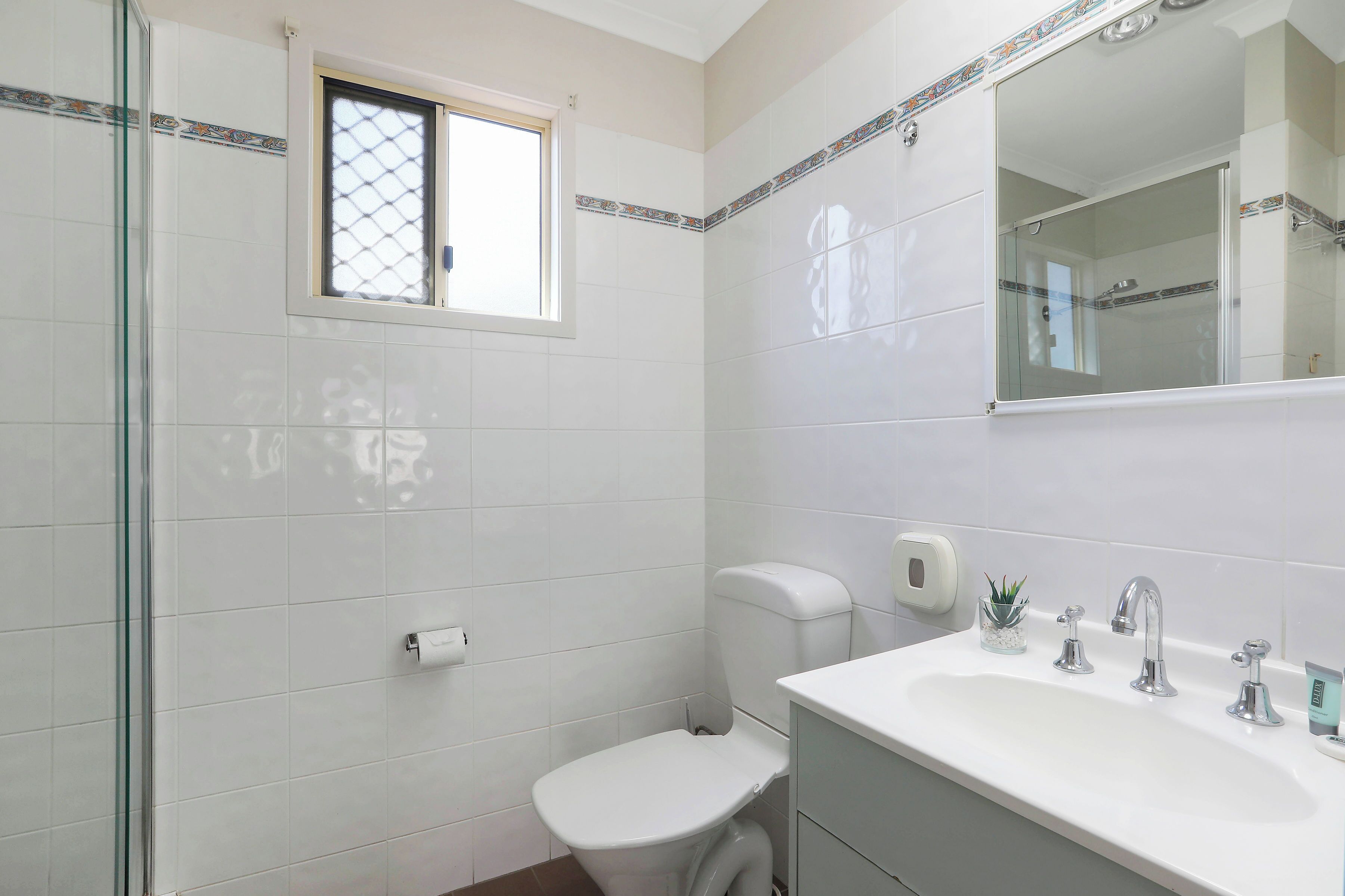 A bathroom with a toilet, sink, and glass shower enclosure.