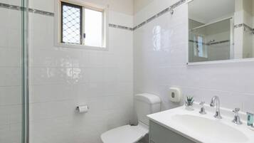A bathroom with a toilet, sink, and glass shower enclosure.