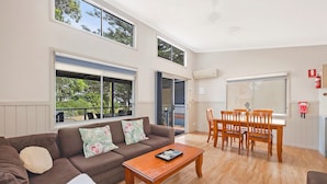 A spacious living room with a brown sofa, a wooden coffee table, and a dining area with a wooden table and chairs.