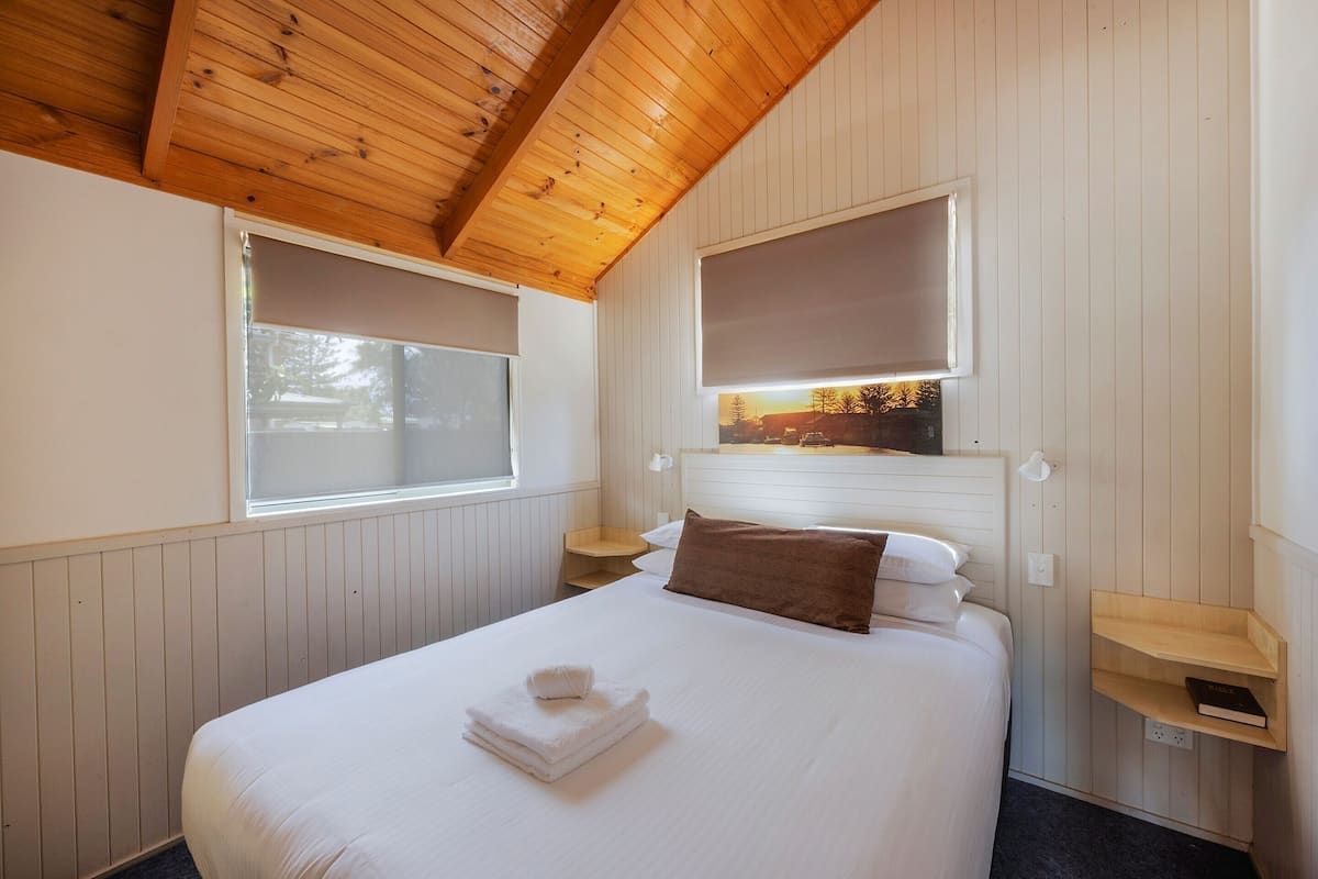 A neatly made bed with a folded towel, two bedside tables, and a headboard with a mounted picture.