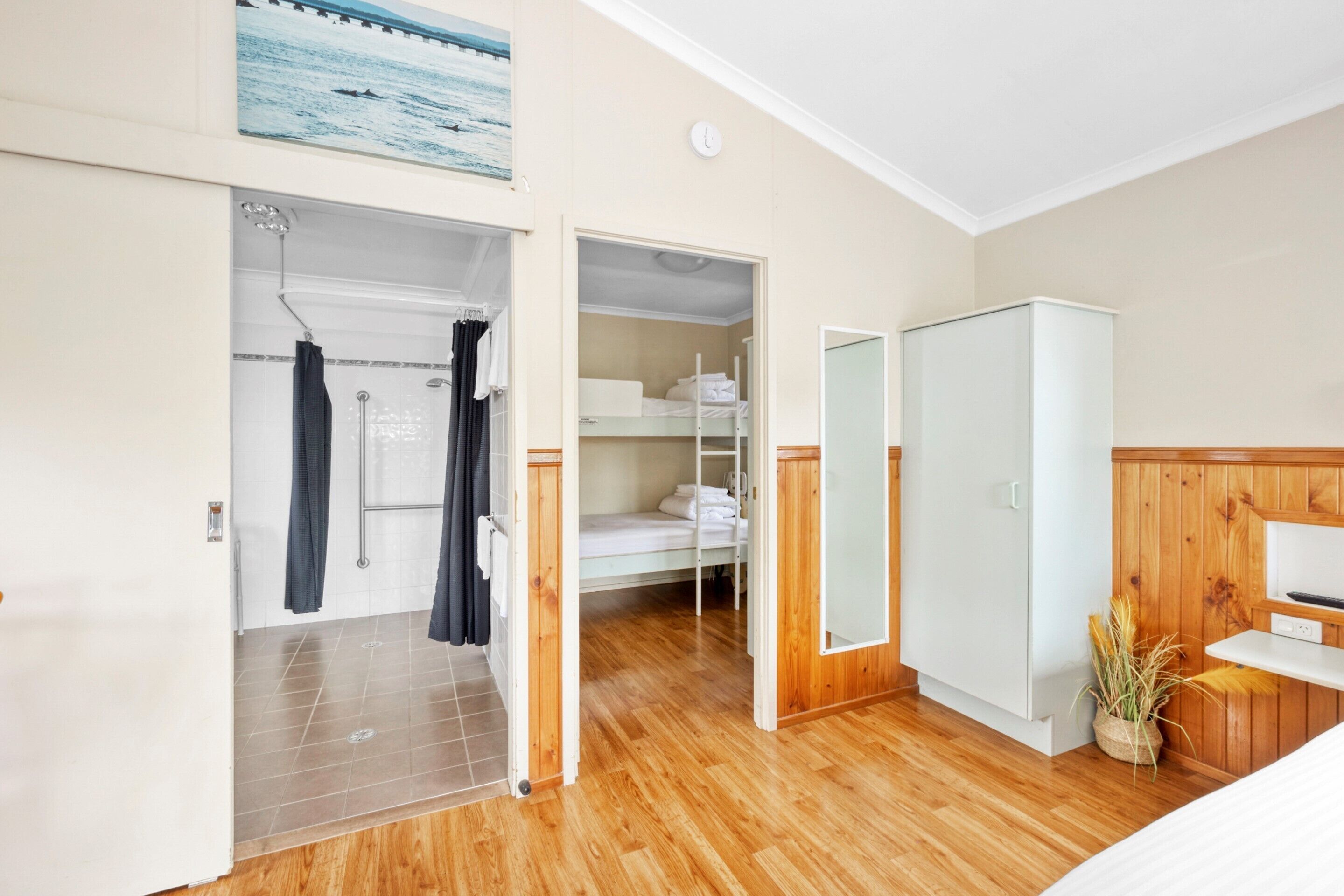 Habitación de hotel con piso de madera, un armario, cama y baño con ducha y cortinas.