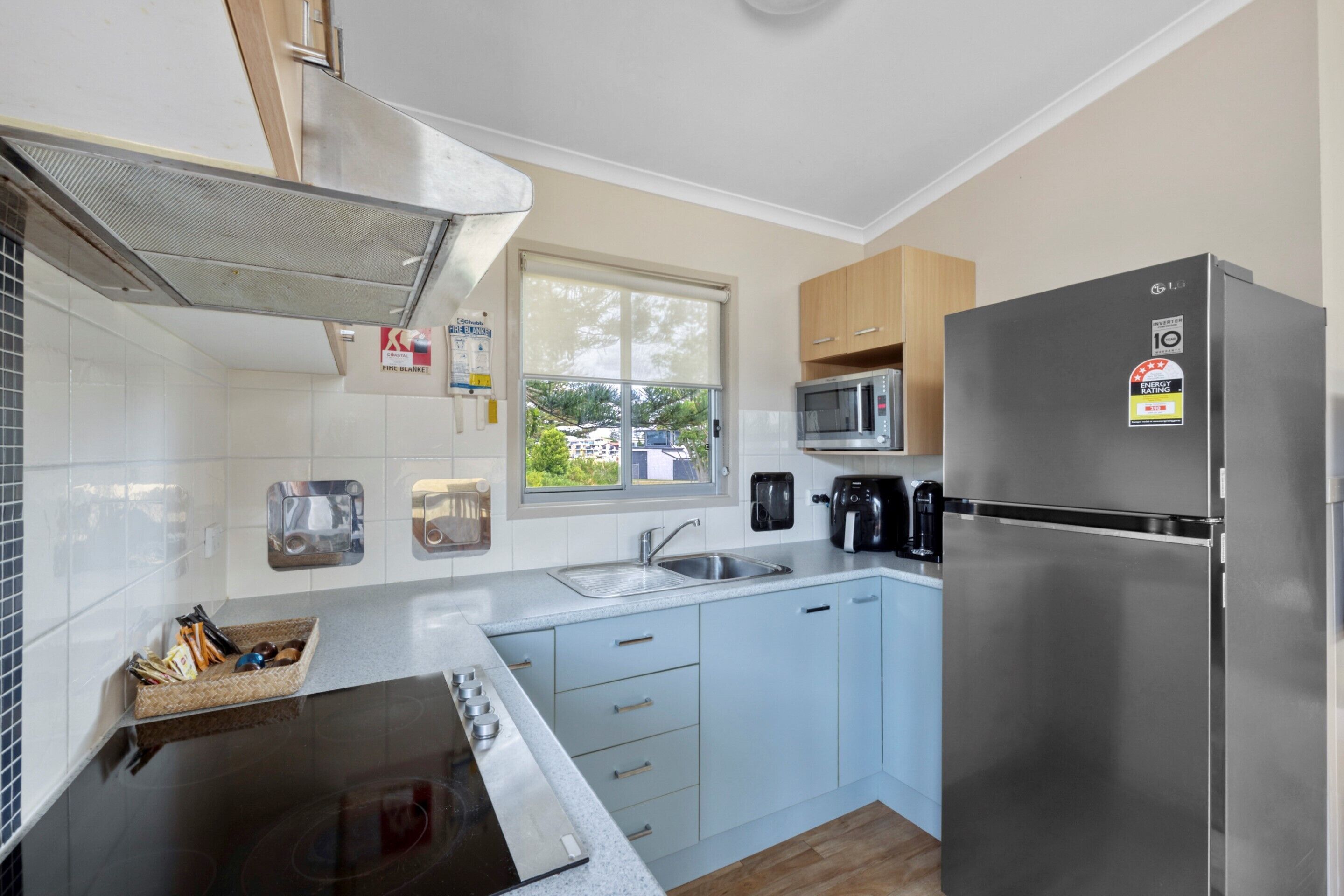 Cocina compacta con refrigerador de acero inoxidable, microondas y estufa. Cuenta con ventana que proporciona luz natural y vistas al exterior.