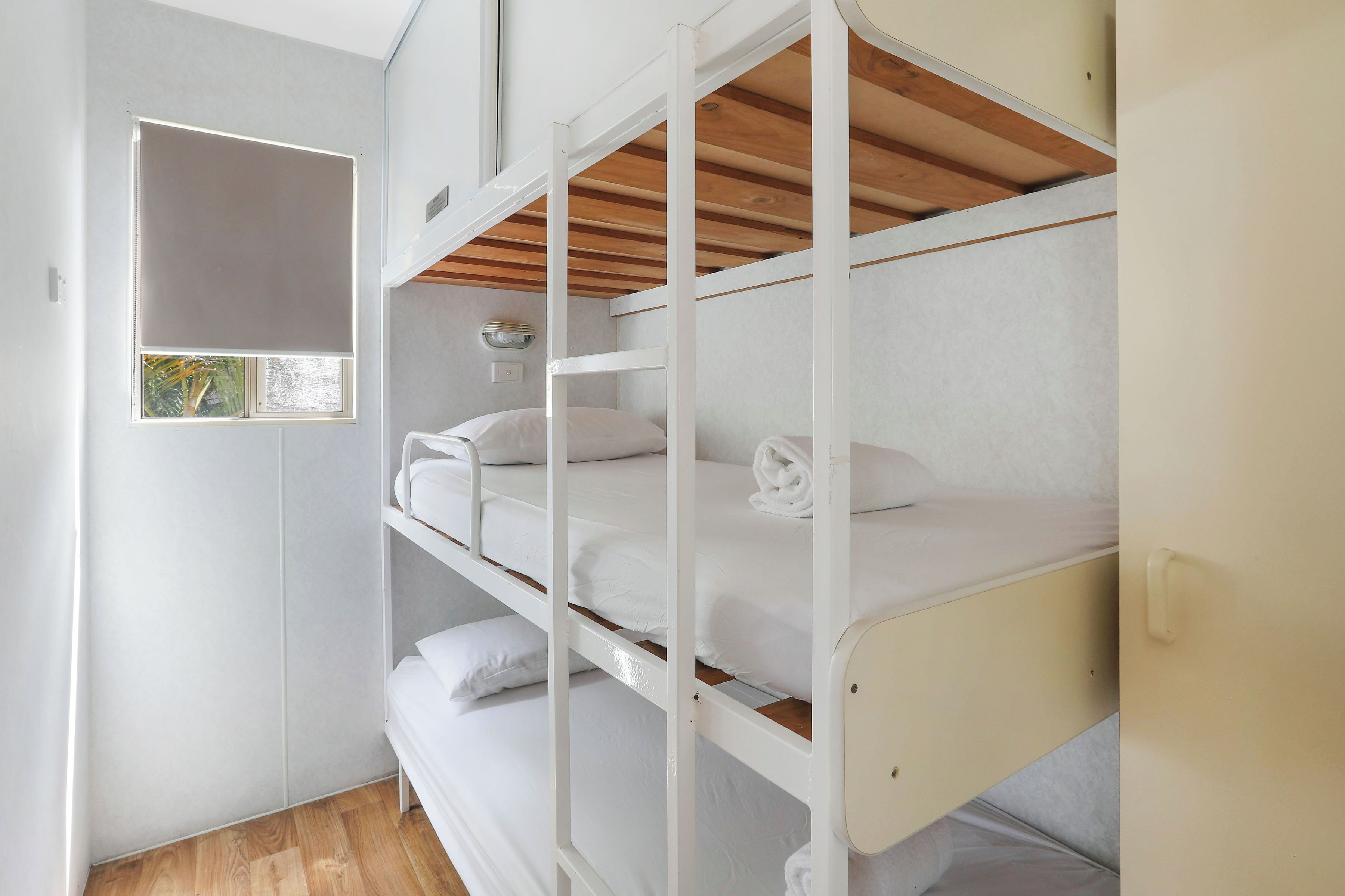 A bunk bed room with white bedding and a small window.