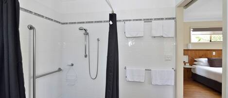 A bathroom with white tiled walls, a shower with a handheld showerhead, a grab bar, and a towel rack with multiple towels.