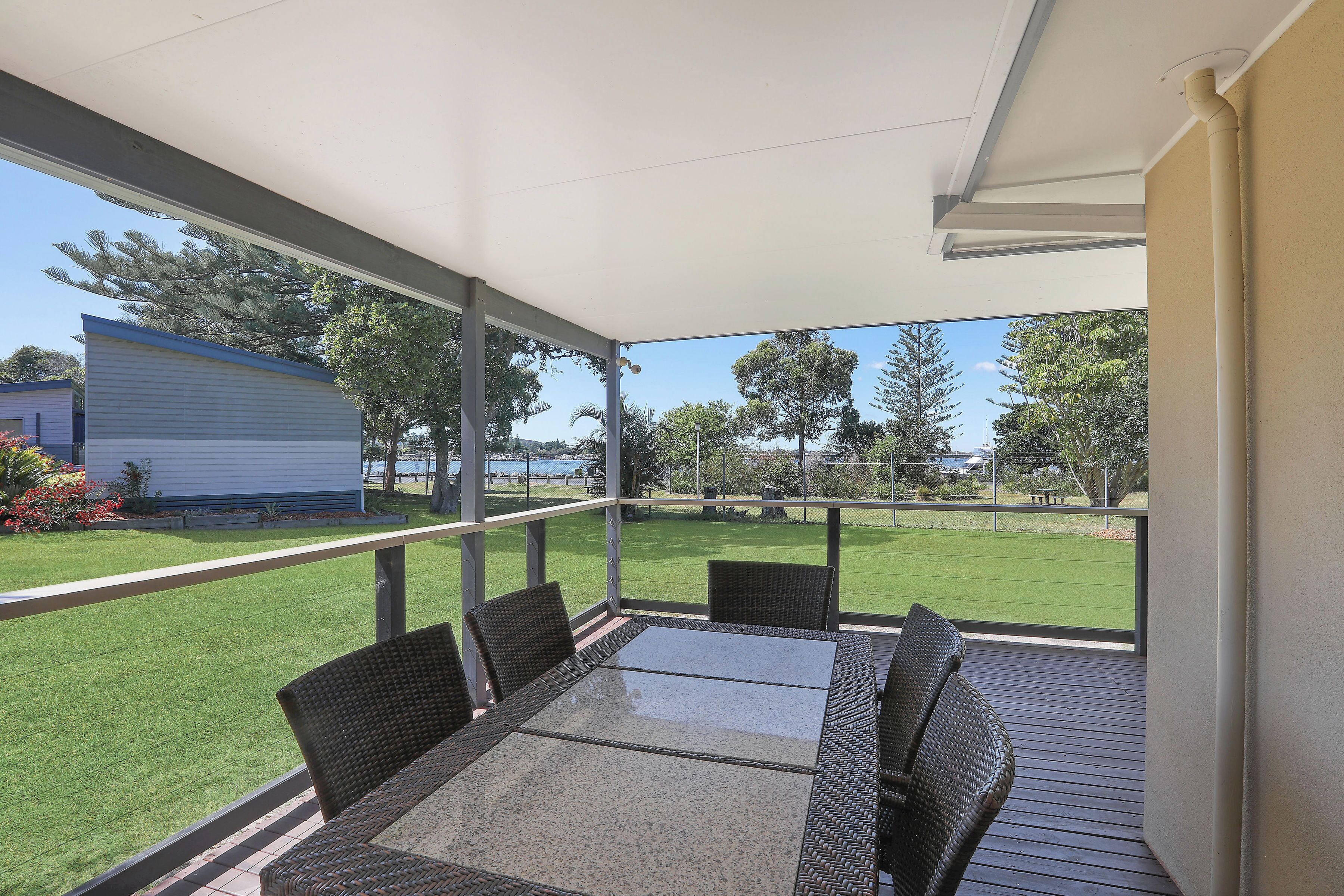 Une terrasse couverte, dotée d’une table et de chaises, qui offre une vue sur une pelouse bien entretenue et un bâtiment situé au loin.