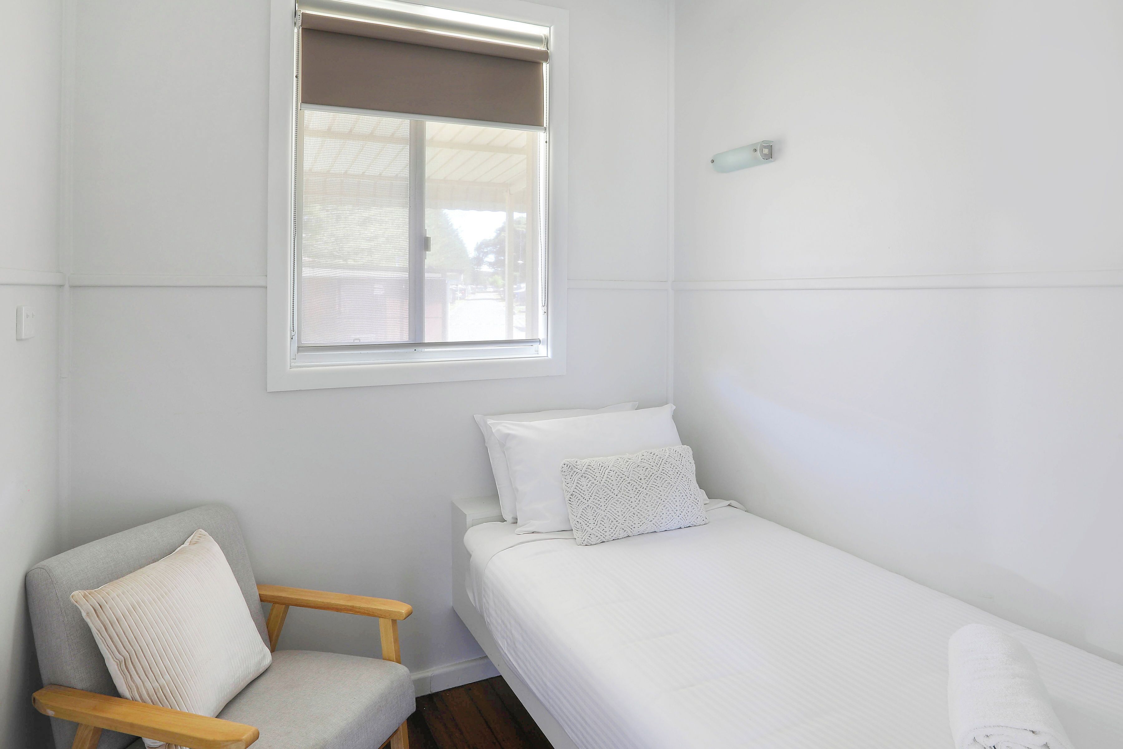 Een kleine, schone kamer met een enkel bed, een stoel en een raam met jaloezieën.