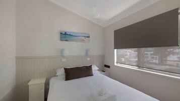 A hotel room with a bed, a nightstand, a wall-mounted lamp, a window with a view, and a painting on the wall.