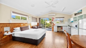 A modern hotel room with a large bed, a desk, a kitchenette, and a balcony with a view.