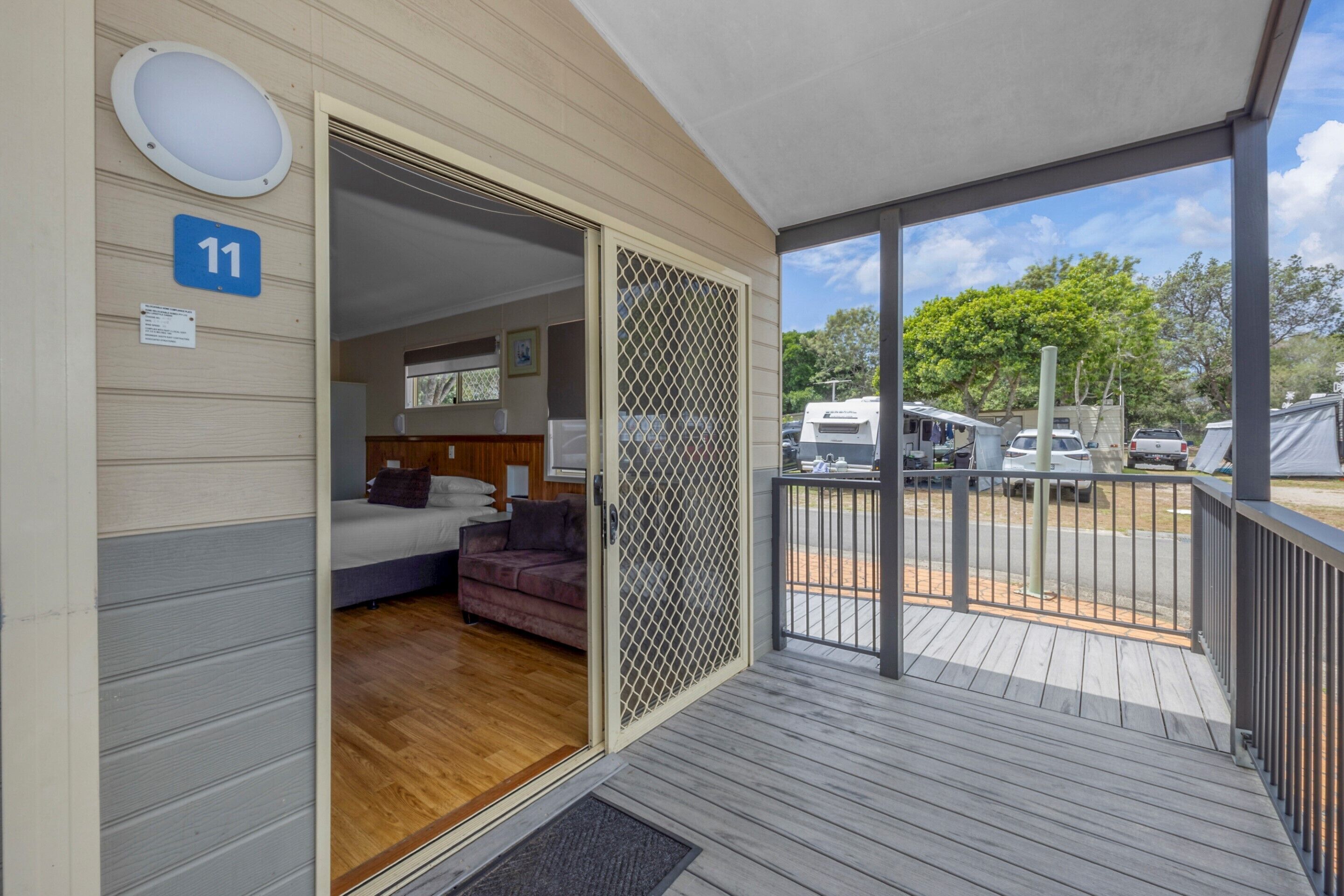 A room with a bed, a couch, and a wooden floor. There is a balcony with a railing and a view of the outside.