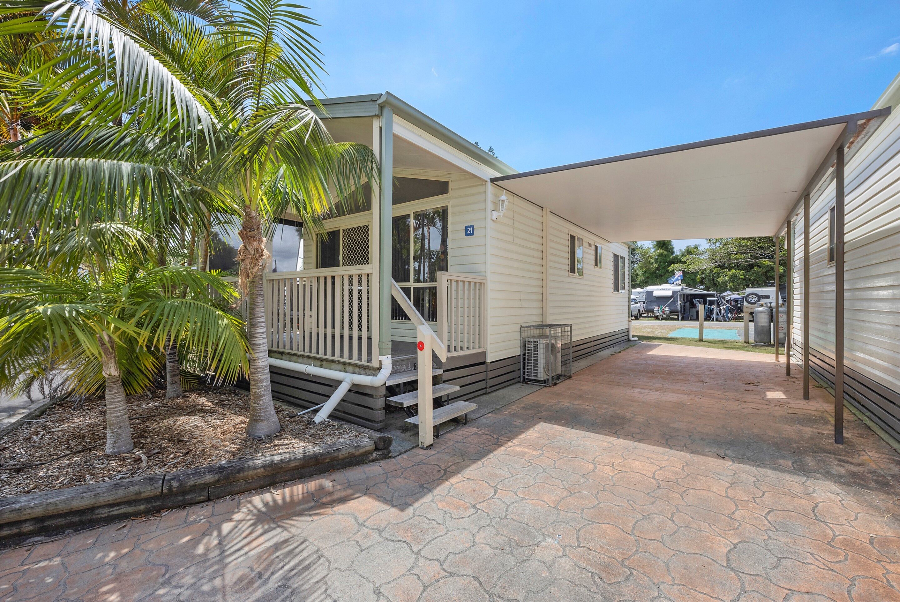 A mobile home with a covered porch, a small deck, and a paved driveway.