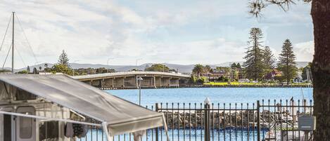 A waterfront view with a bridge, a boat, and a fenced area with a tent.