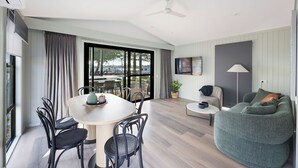 A modern living room with a dining area, large windows, and a ceiling fan. - Reflections Forster Beach - Holiday Park (Forster)