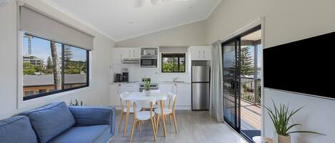 A modern kitchen with white cabinets, a microwave, and a refrigerator. There is a dining table with chairs and a blue sofa in the living area.
