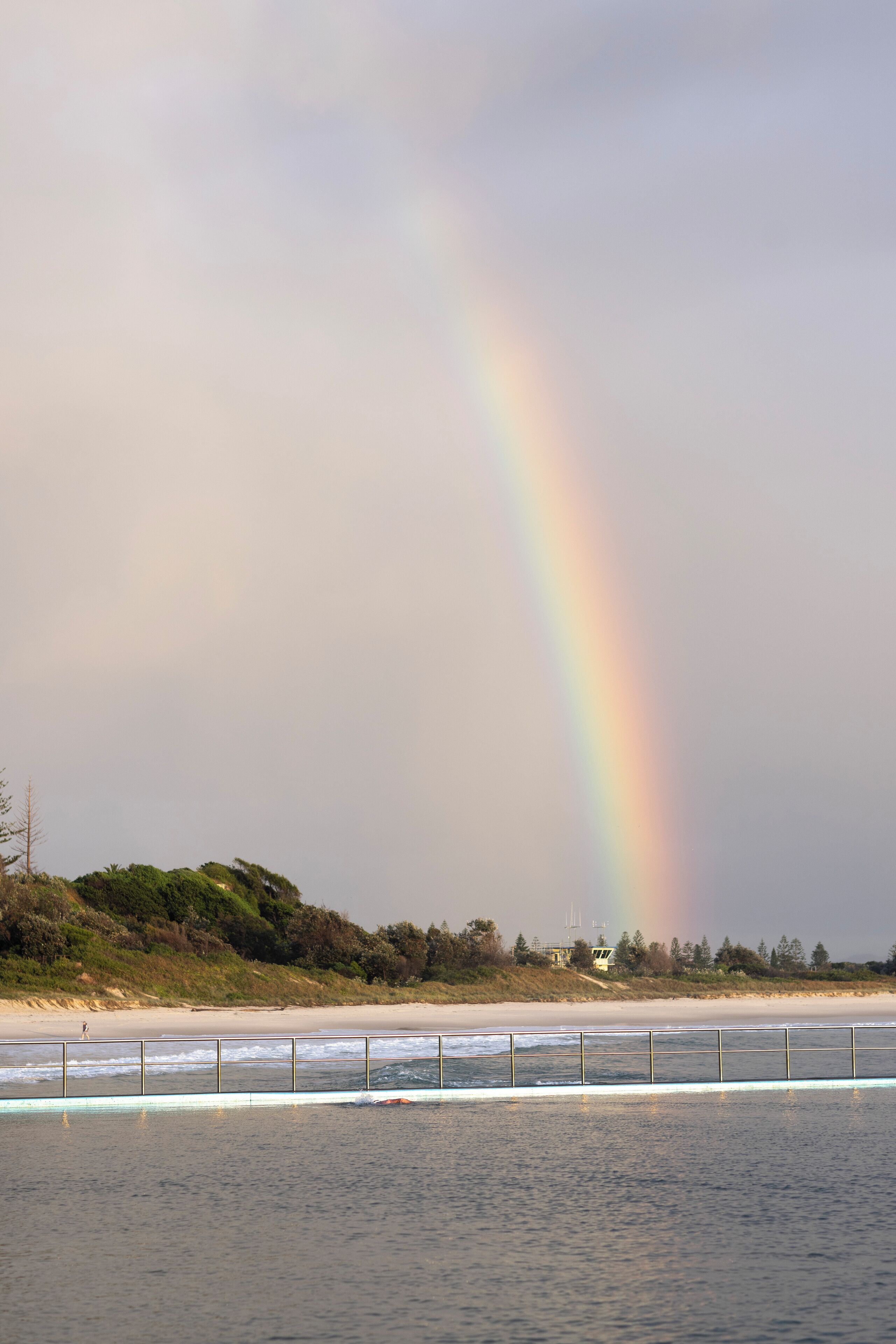 A beach with a rainbow, a sandy shore, and a body of water.