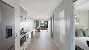 A modern kitchen with a built-in water dispenser, a dining area with a table and chairs, and a bedroom with a bed and a view of the outside. - Reflections Forster Beach - Holiday Park (Forster)