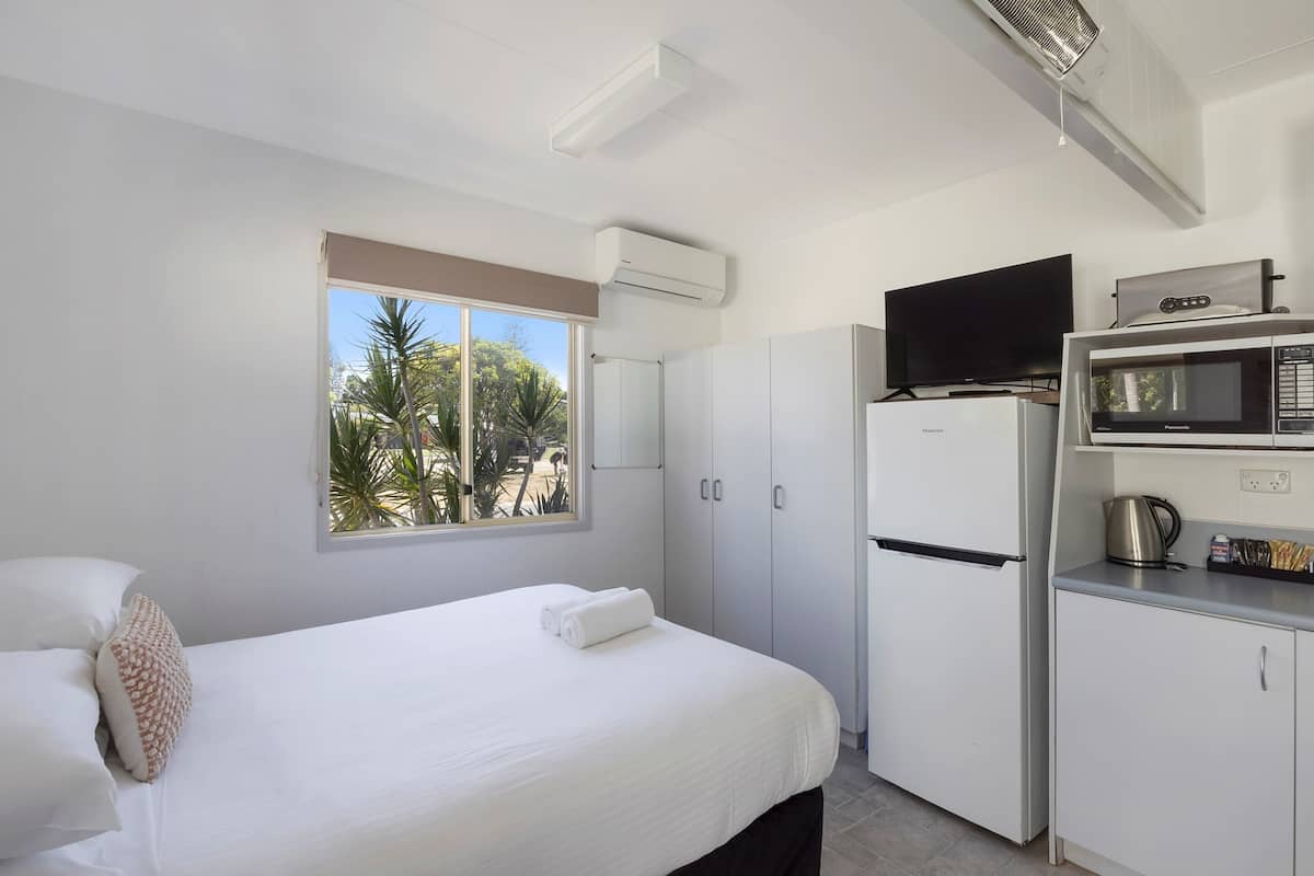 Una habitación de hotel con una cama, televisión, microondas y kitchenette.