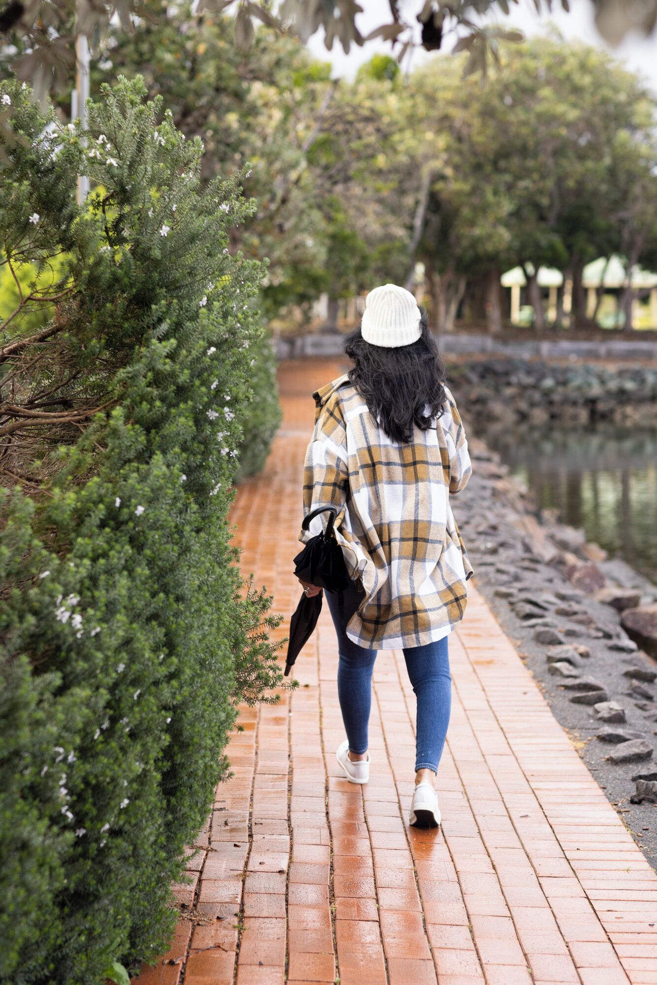 A person walking on a brick pathway beside a body of water, surrounded by greenery.