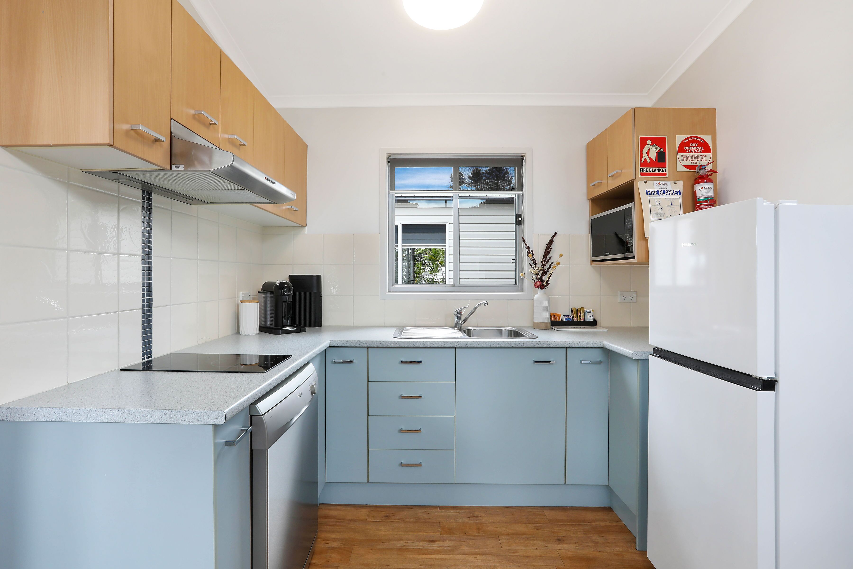 Una cocina compacta con armarios azul claro, un refrigerador blanco y una ventana sobre el fregadero.