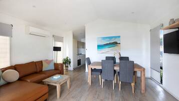A modern living room with a brown leather sofa, a wooden coffee table, and a dining area with a wooden table and grey chairs.