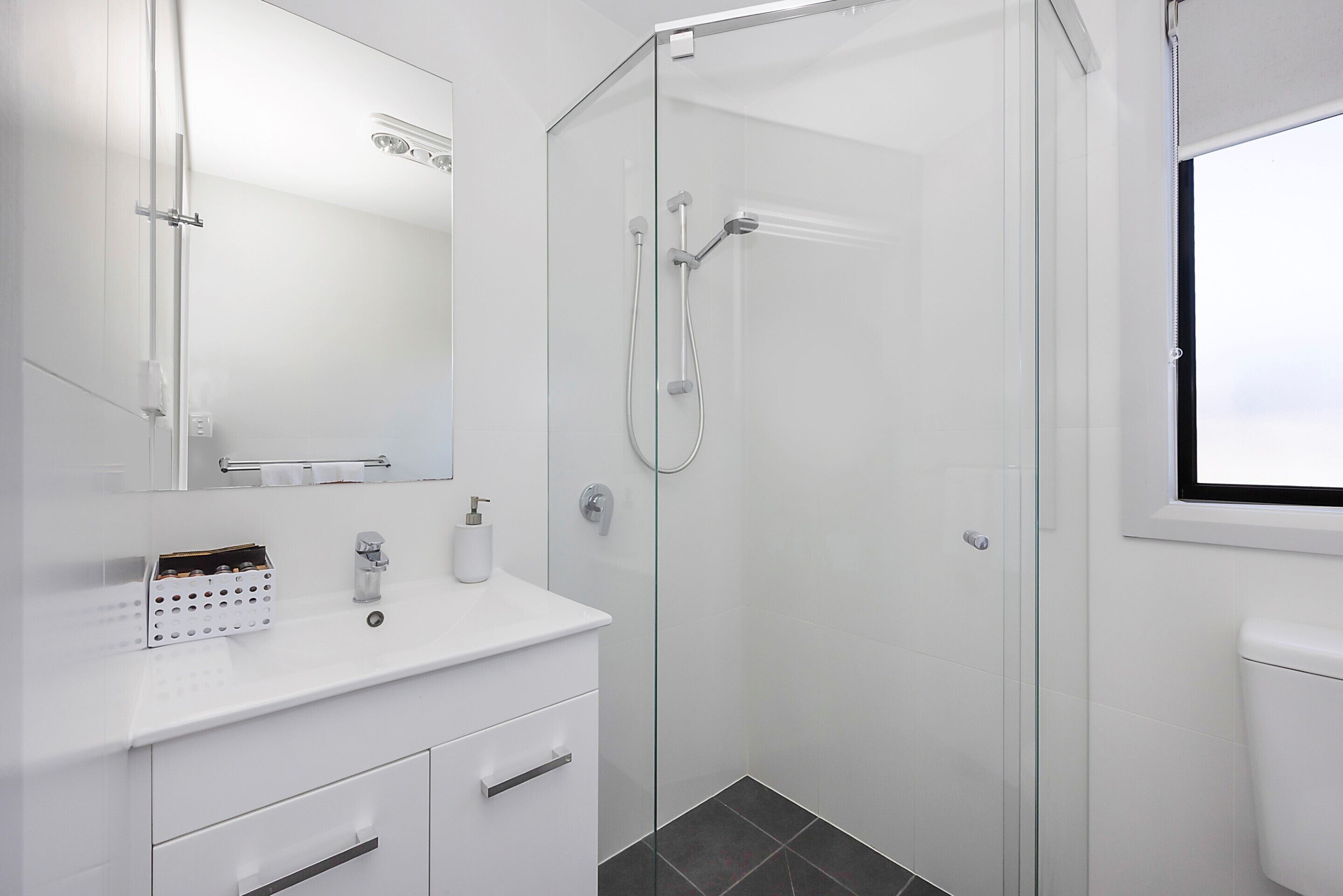A modern bathroom with a glass-enclosed shower, white fixtures, and a large mirror.