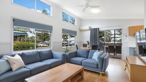A modern living room with a sectional sofa, a wooden coffee table, and a dining area with a table and chairs. - Reflections Forster Beach - Holiday Park (Forster)