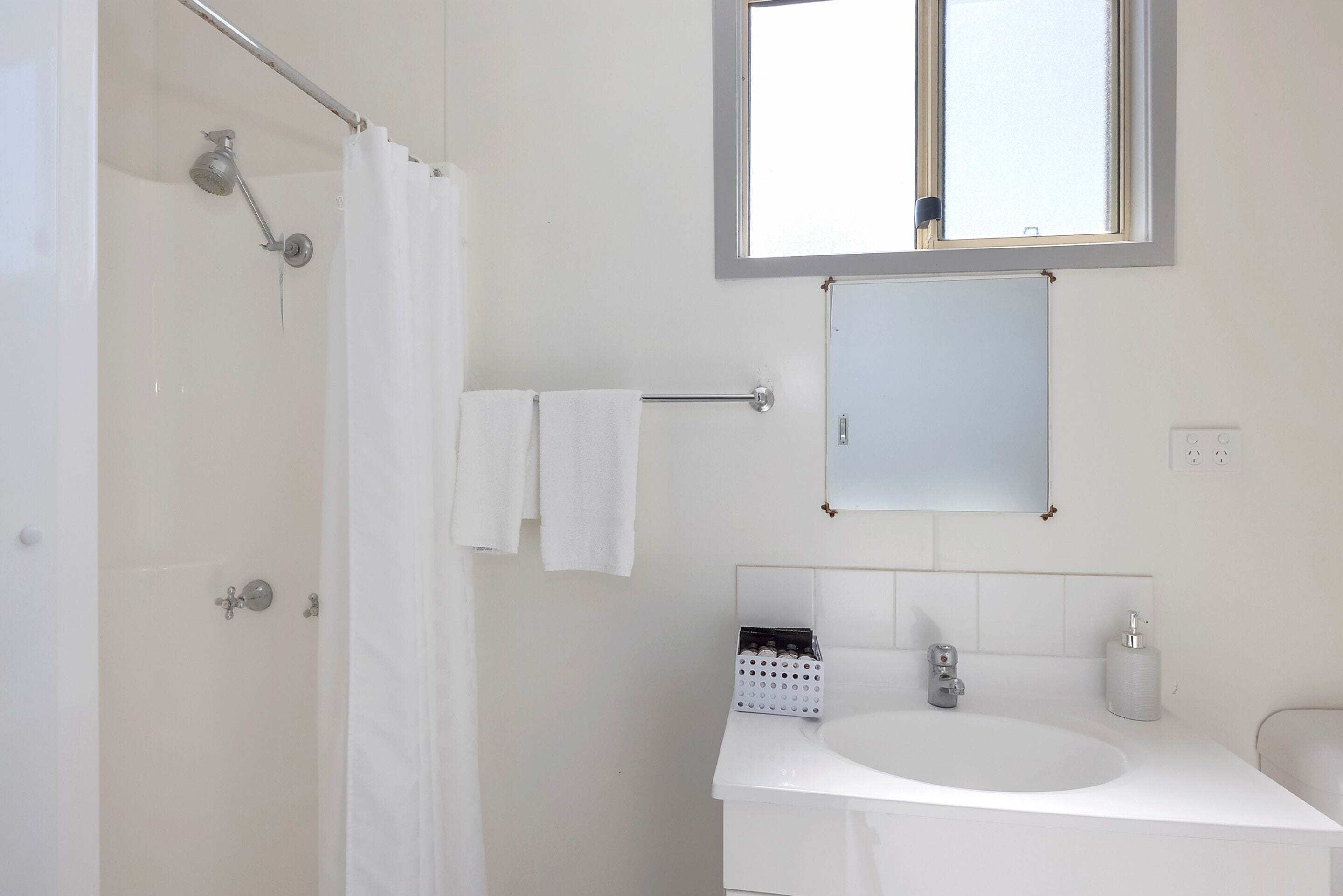 Une salle de bain avec une douche, un lavabo, un miroir et une fenêtre.