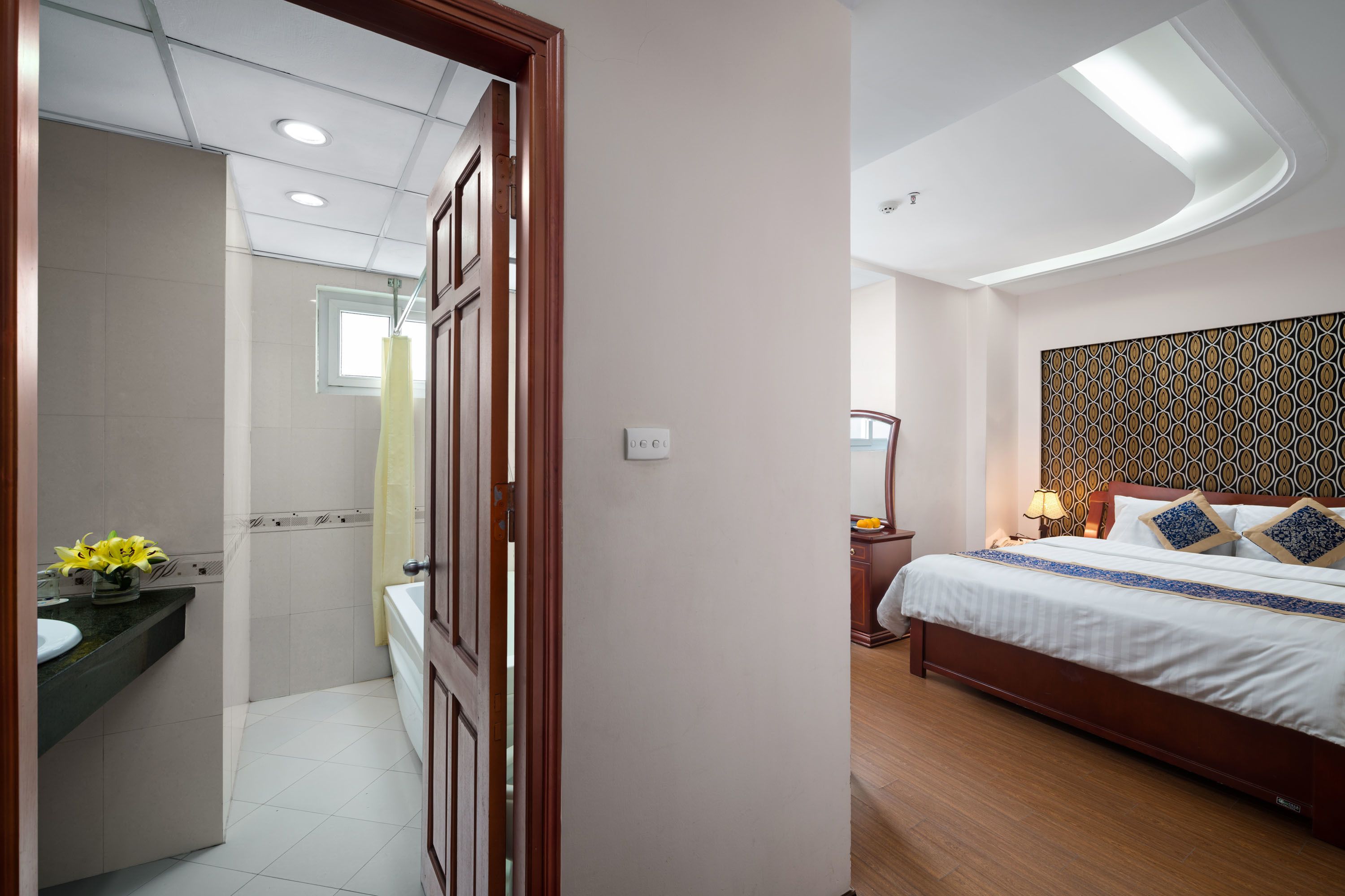 A hotel room with a bed, bedside table, and a bathroom with a sink and mirror.