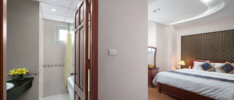 A hotel room with a bed, bedside table, and a bathroom with a sink and mirror.