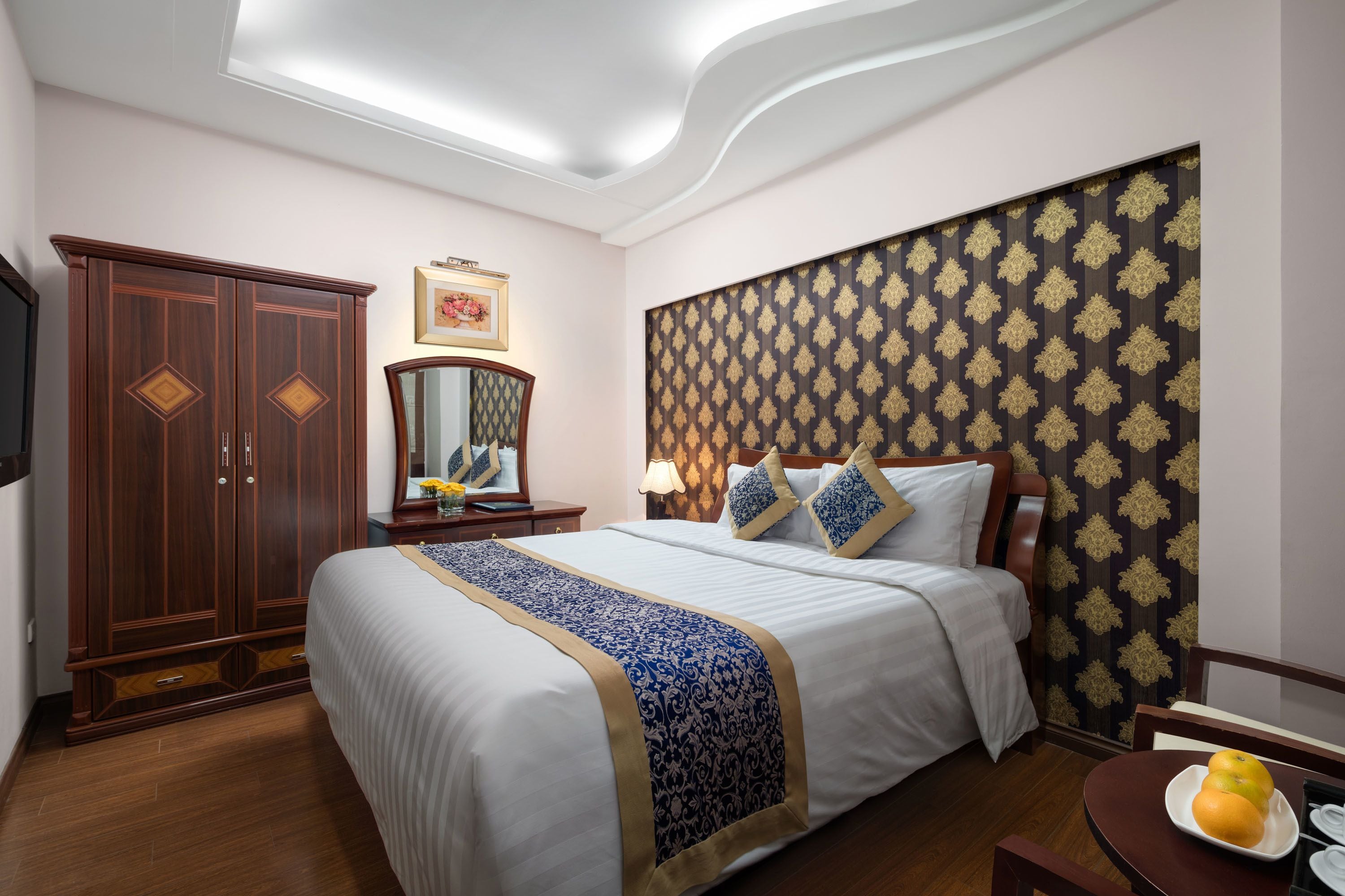 Habitación de hotel con una cama grande, un armario, una mesita de noche con lámpara y un papel tapiz estampado en la pared.
