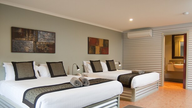 Ein Hotelzimmer mit zwei Betten, einem großen abstrakten Gemälde und einem durch eine offene Tür einsehbaren Badezimmer.