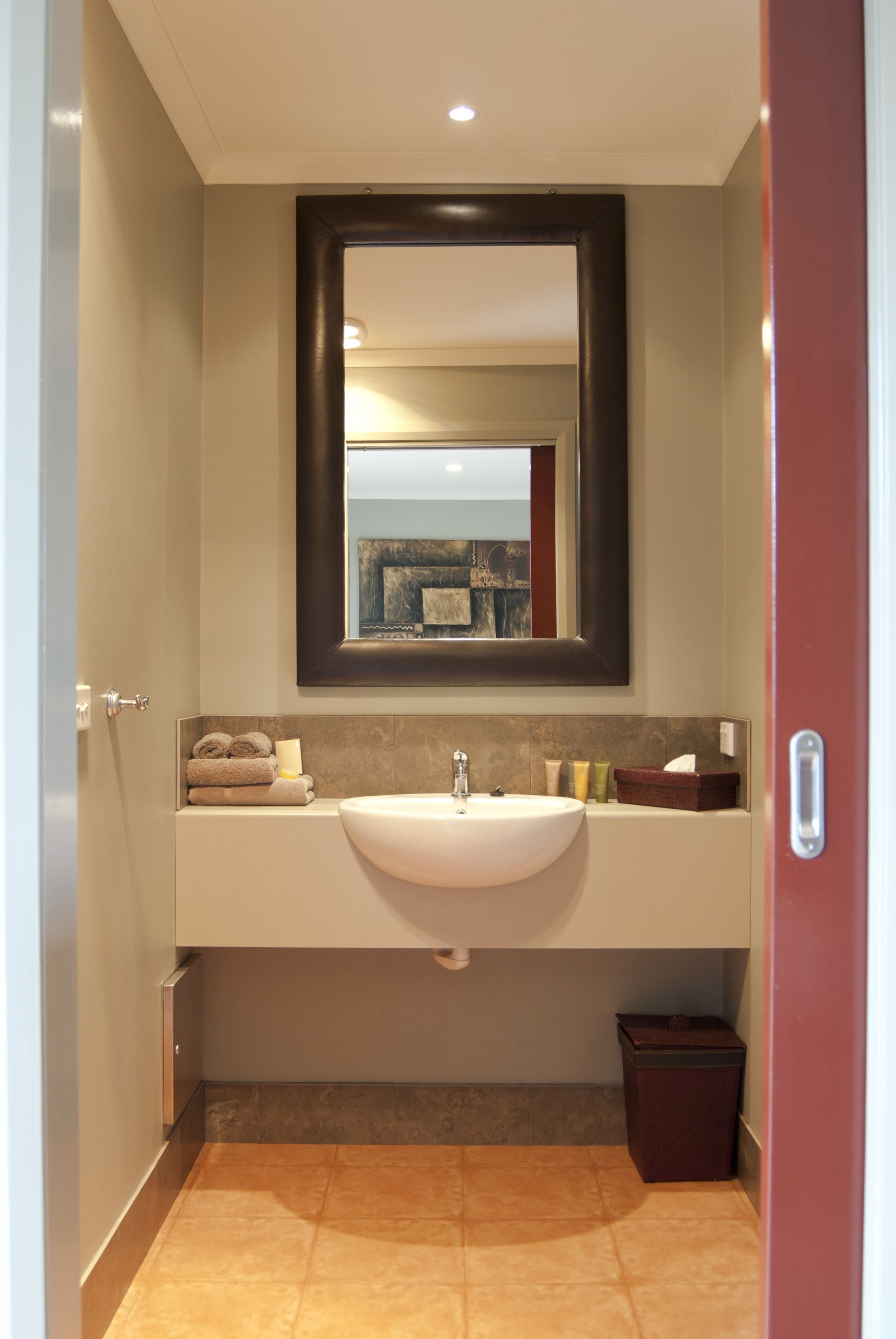Un baño con lavamanos blanco, espejo y cubo de basura.