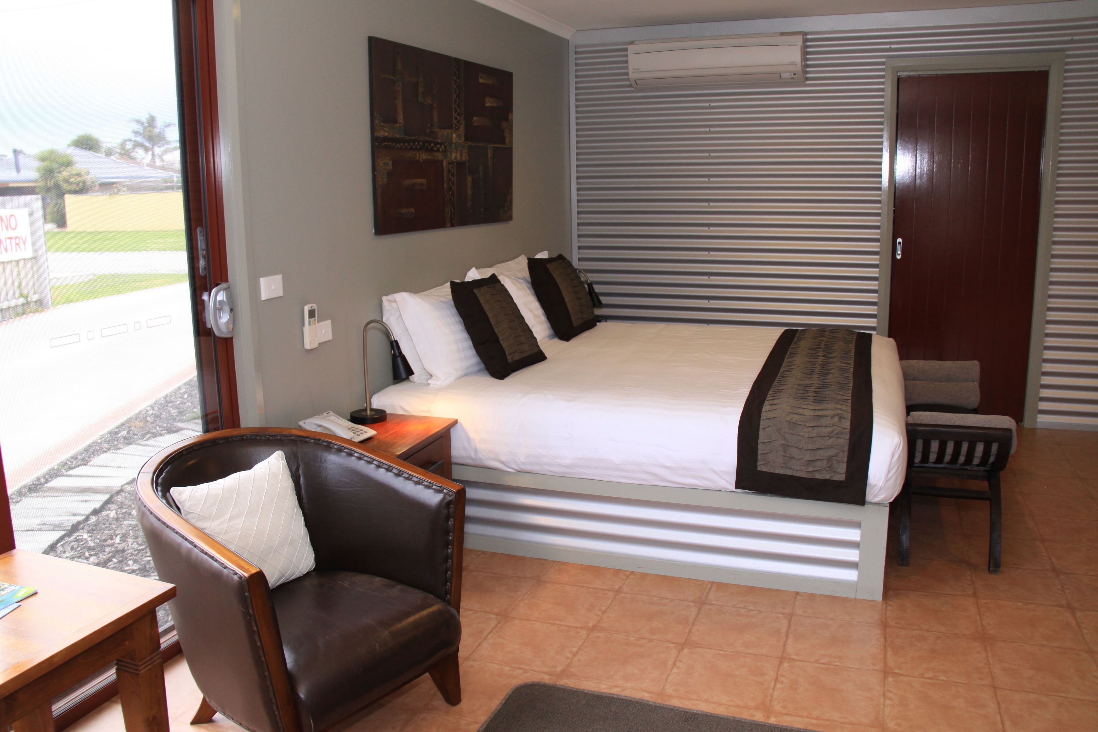 A bedroom with a large bed, a chair, a desk, and a door.