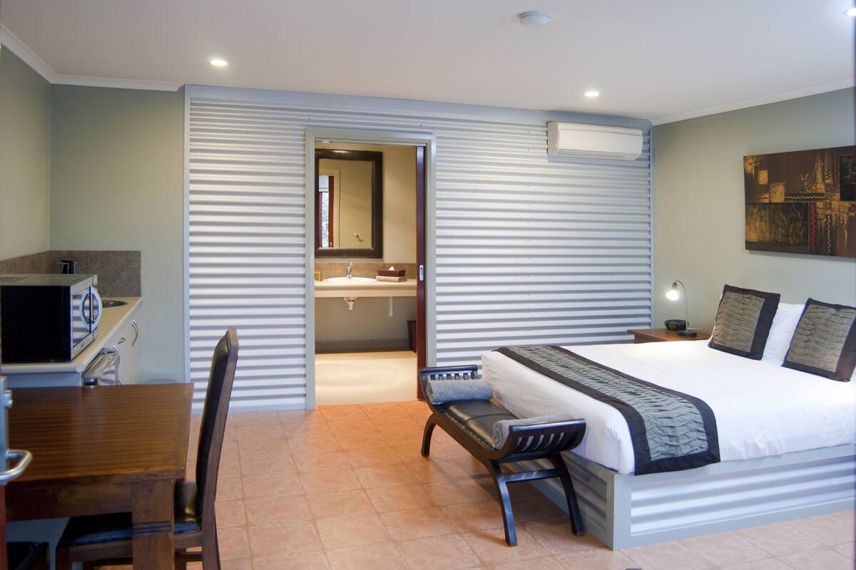 Une chambre d’hôtel avec un lit, un bureau, une chaise, une salle de bain et un tableau au mur.