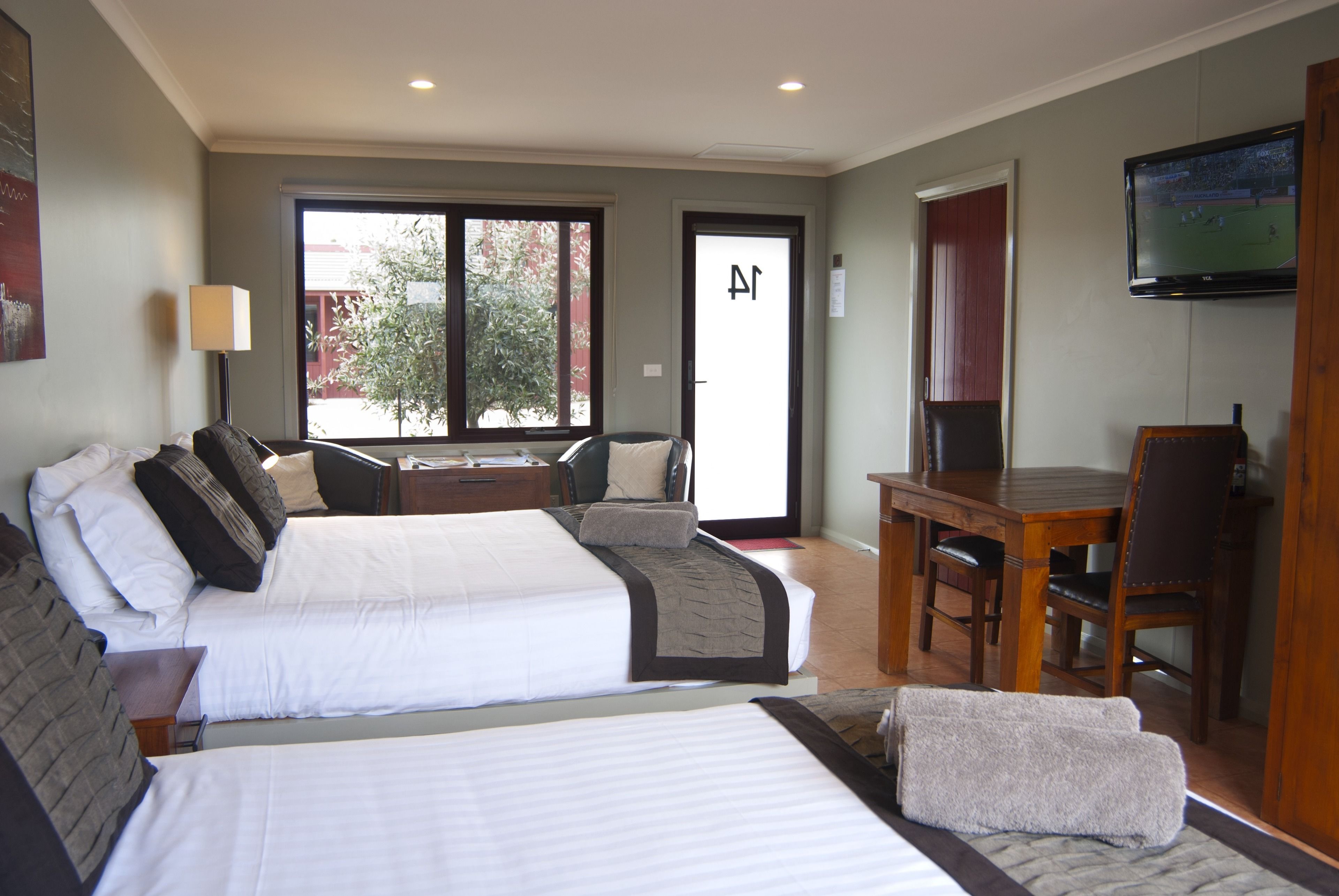 A hotel room with two beds, a dining table, a TV, and a sliding glass door to the outside.