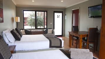 Quarto de hotel com duas camas, uma mesa de jantar, uma televisão e uma porta de correr de vidro para o exterior.