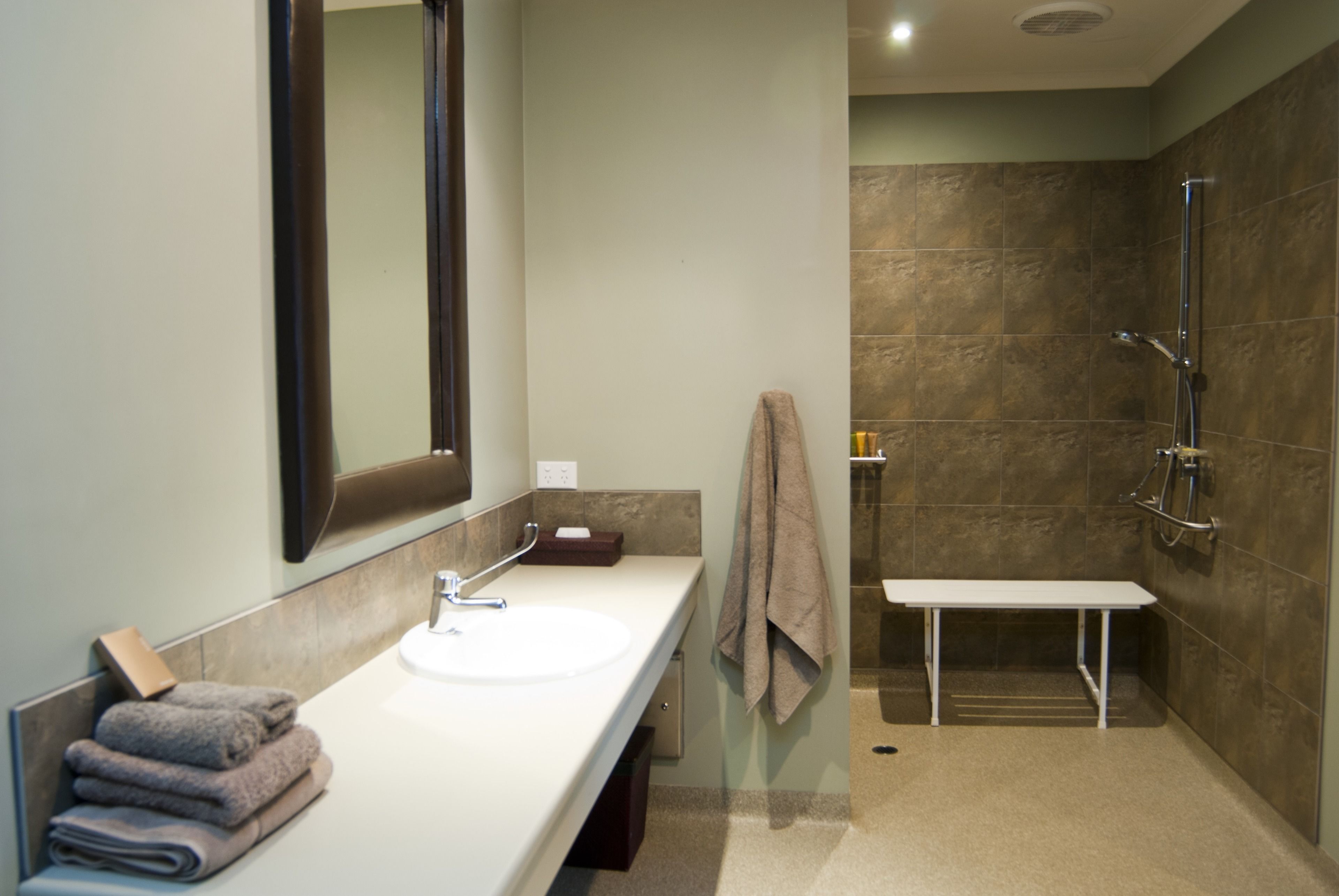 A modern bathroom with a white sink, a large mirror, a towel rack, and a shower area.