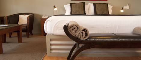 A hotel room with a bed, a bench with a rolled towel, a desk, and a chair.