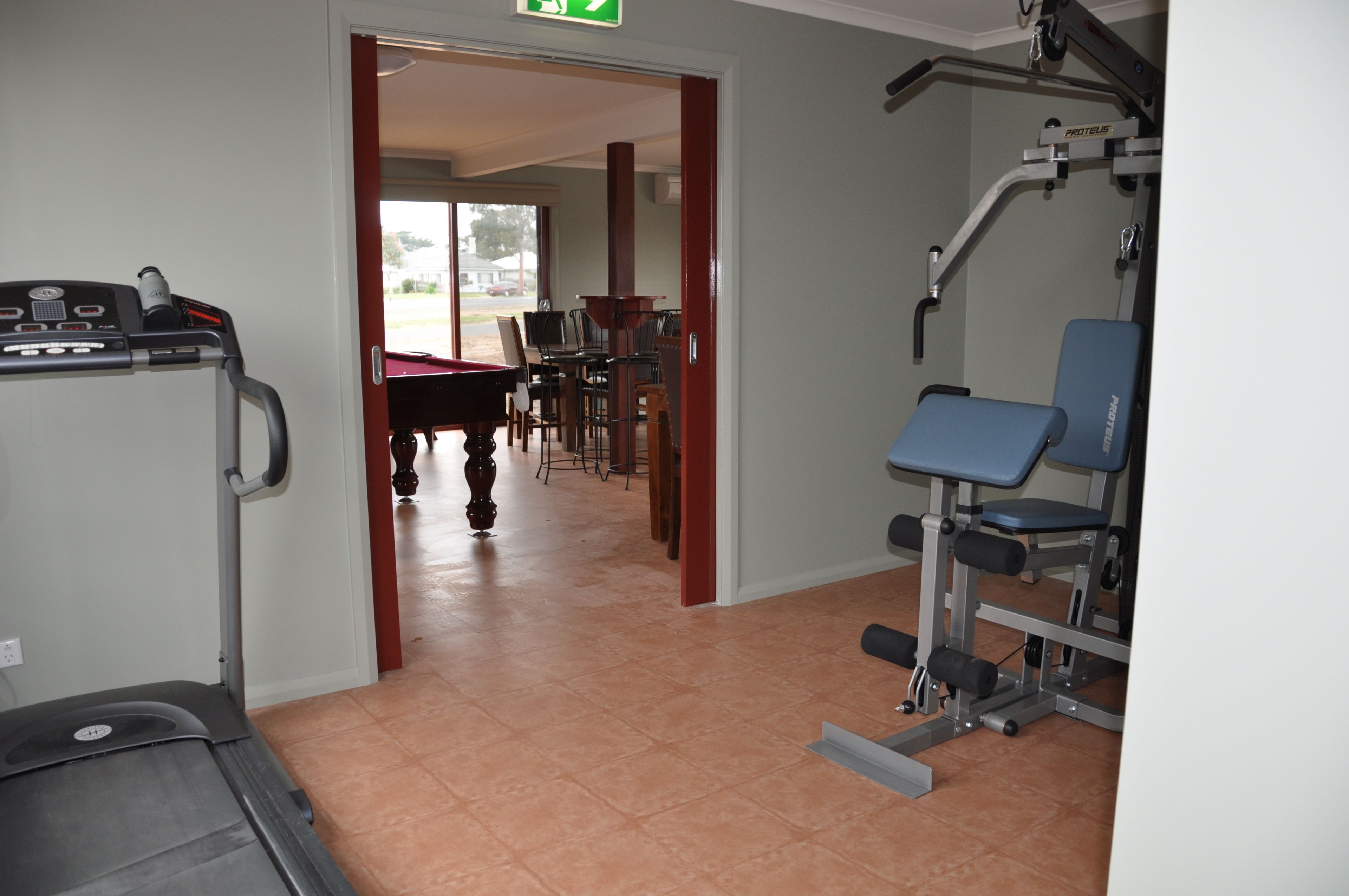 Ein Fitnessraum mit Trainingsgeräten, ein Billardtisch und ein Essbereich mit Stühlen und Tischen.