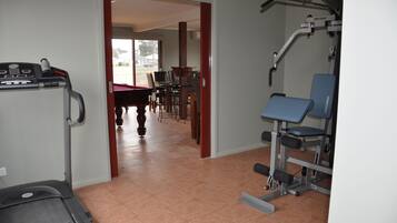 Een sportschool met fitnessapparatuur, een pooltafel en een eetgedeelte met stoelen en tafels.