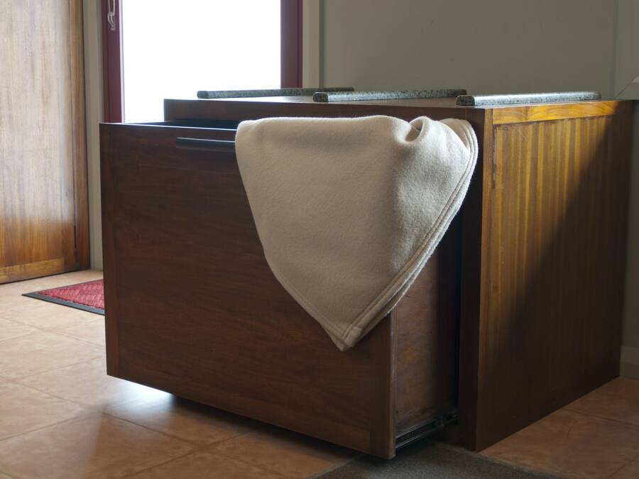 A wooden dresser with a beige towel draped over it, situated in a room with tiled flooring and a window in the background.