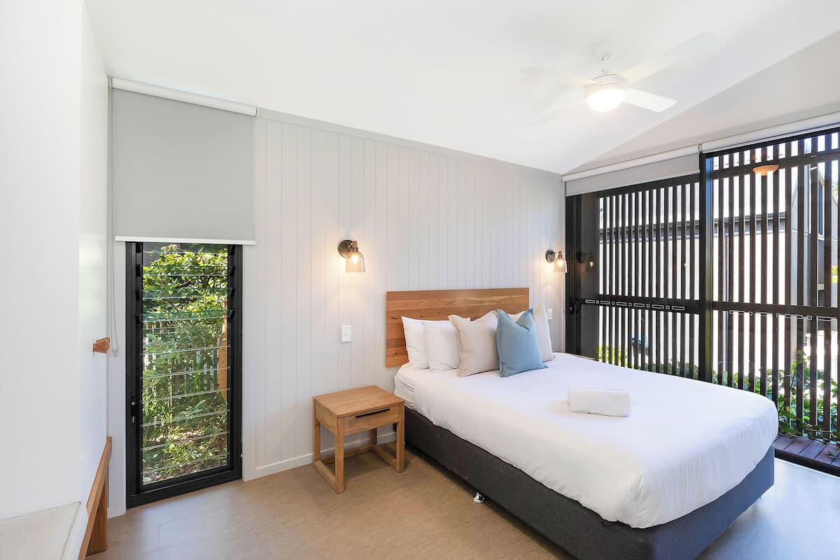 A bedroom with a bed, a small wooden nightstand, a ceiling fan, and a sliding glass door leading to a balcony.