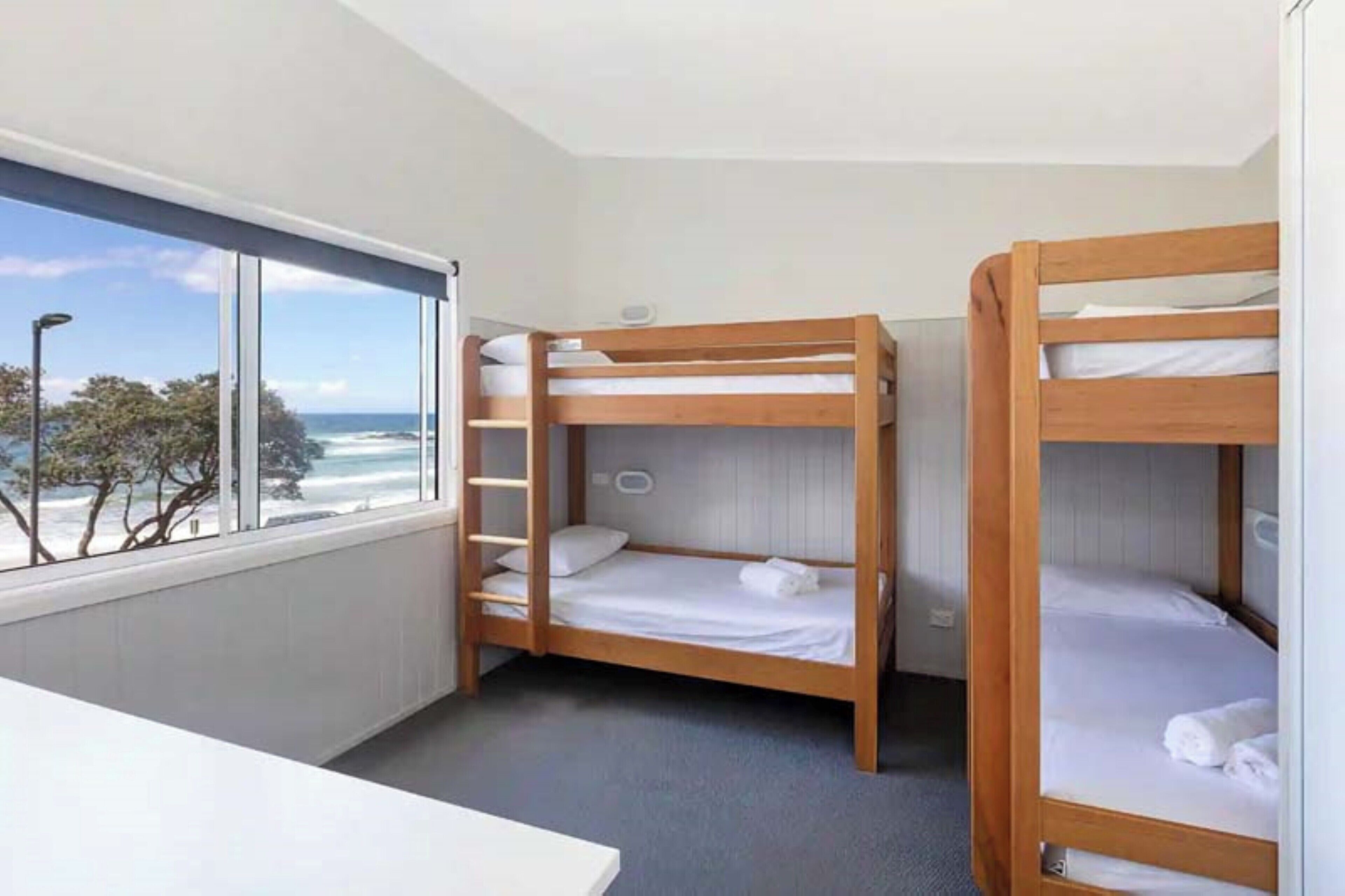 A room with three bunk beds, a window with a view of the ocean, and a small table.