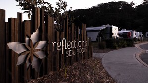 Een houten bord met de tekst 'reflections seal rocks' en een metalen bloemdesign.