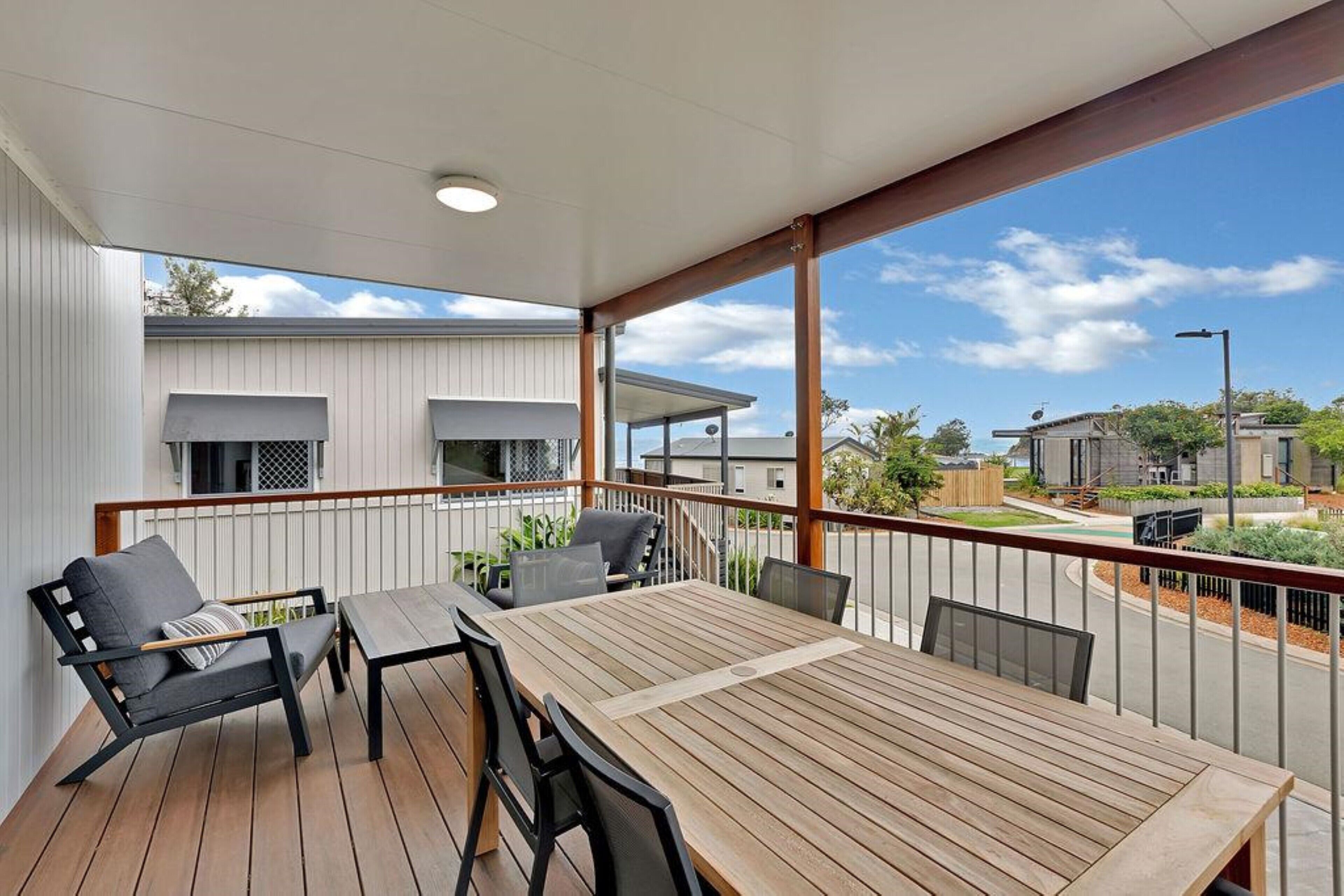 A wooden deck with a table and chairs, a sofa, and a railing overlooking a street.