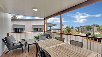Um deck de madeira com mesa, cadeiras, um sofá e guarda-corpo com vista para a rua.