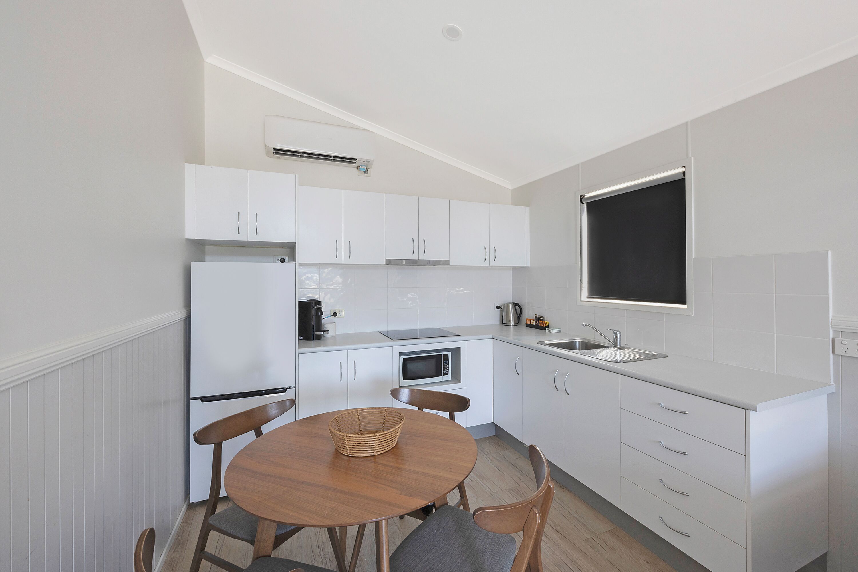 A compact kitchen with white cabinets, a microwave, a sink, and a dining table with chairs.