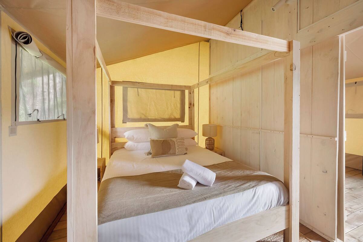 A room with a bed, a window, and a wooden ceiling structure.