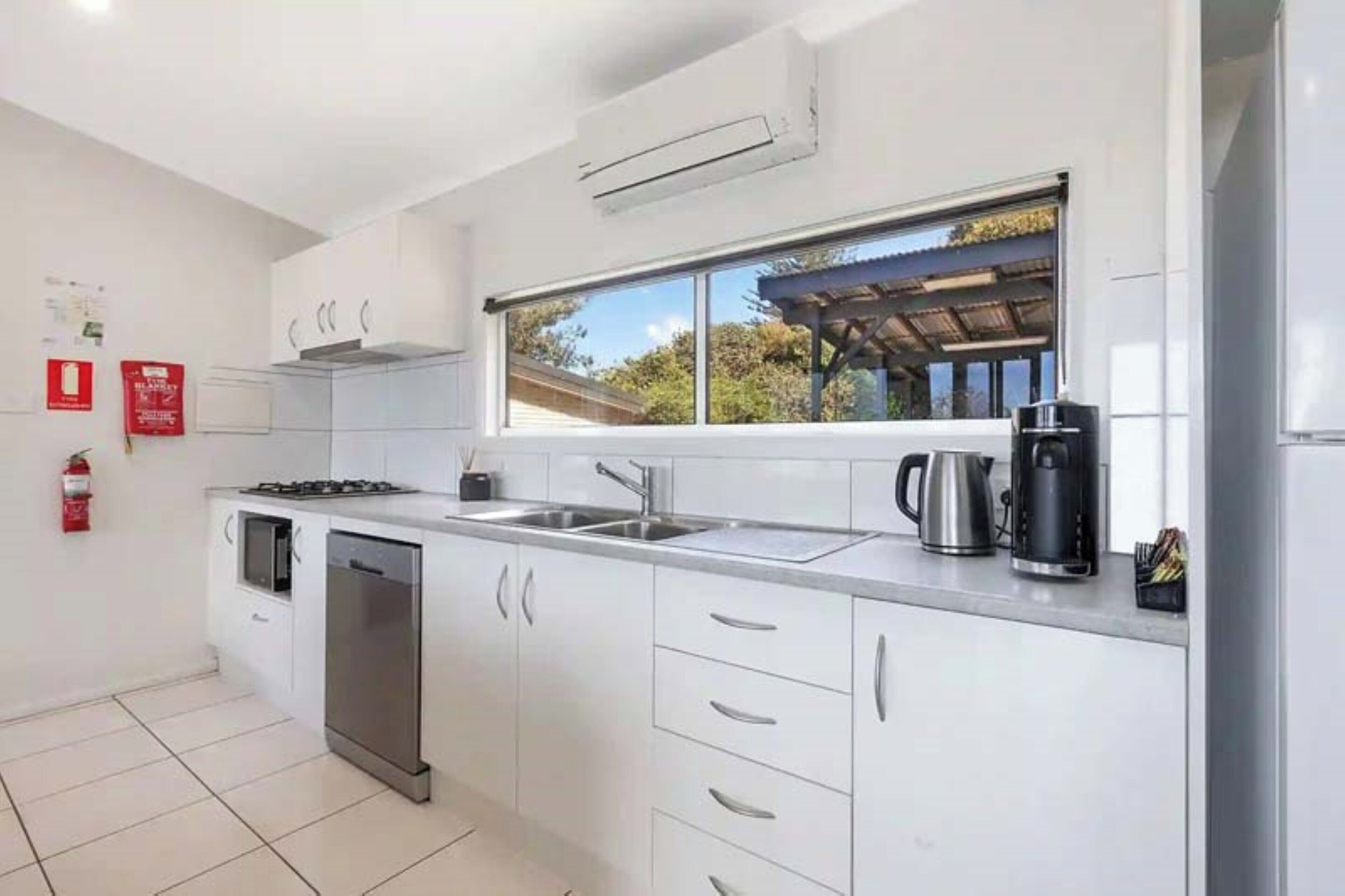 A modern kitchen with white cabinets, stainless steel appliances, a large window, and a fire extinguisher on the wall.