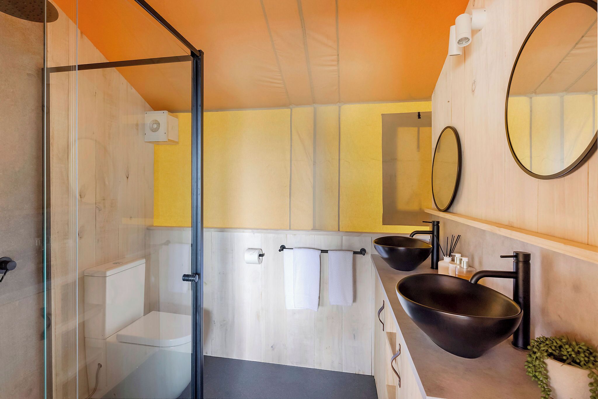 Un bagno moderno con box doccia in vetro, un water, un lavandino con lavabo nero e due specchi.